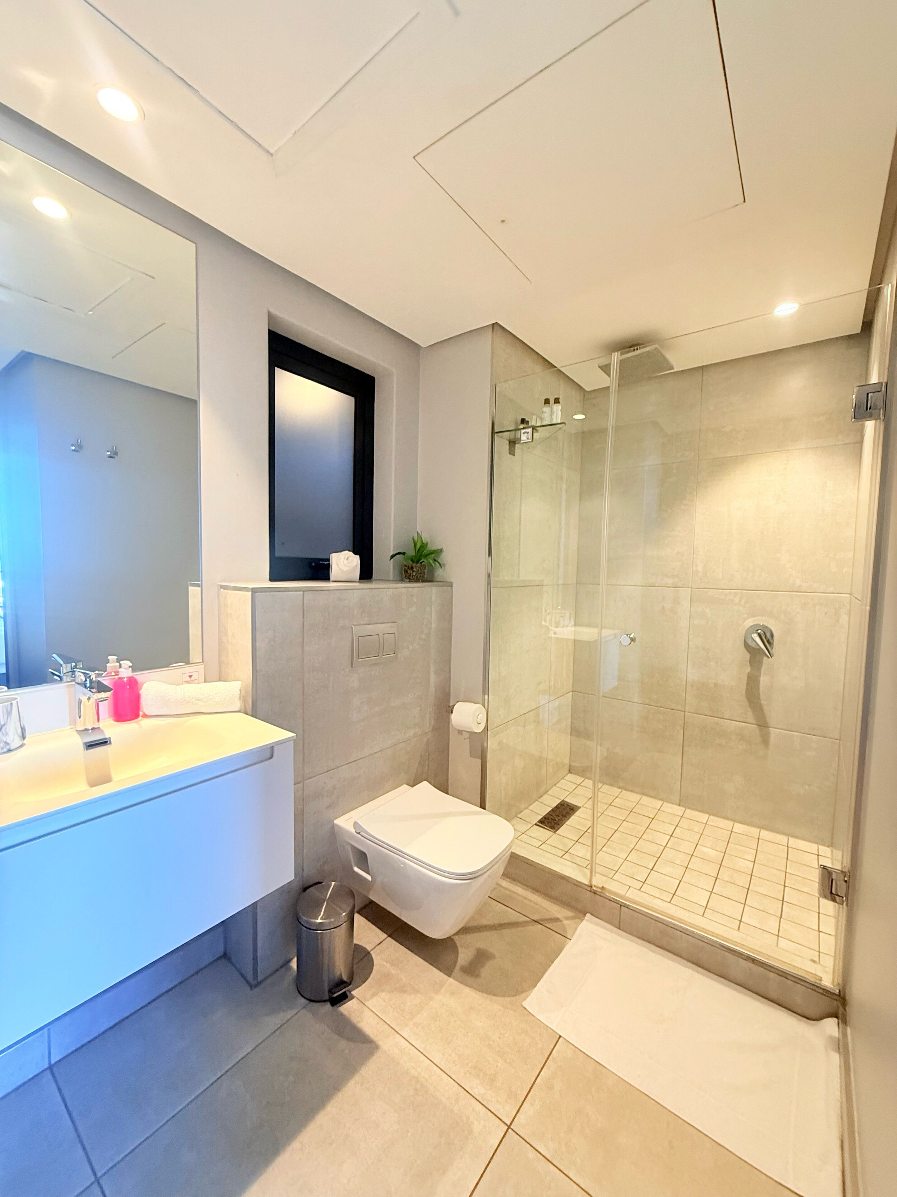 A modern bathroom with a glass-enclosed shower, a white sink, and a large mirror.