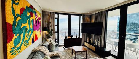 A modern living room with a large window, a sofa, a coffee table, and a flat-screen TV.