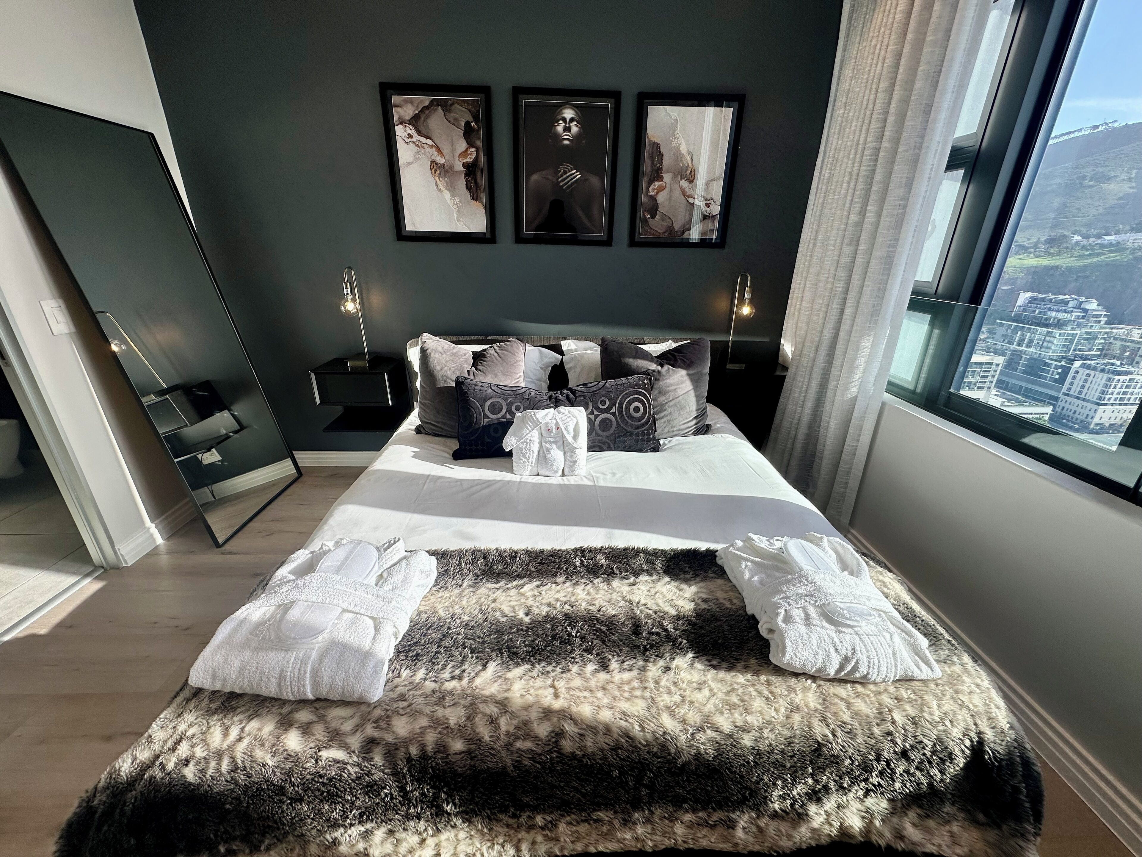 A modern bedroom with a large bed, multiple pillows, a fluffy rug, and framed artwork on the wall.