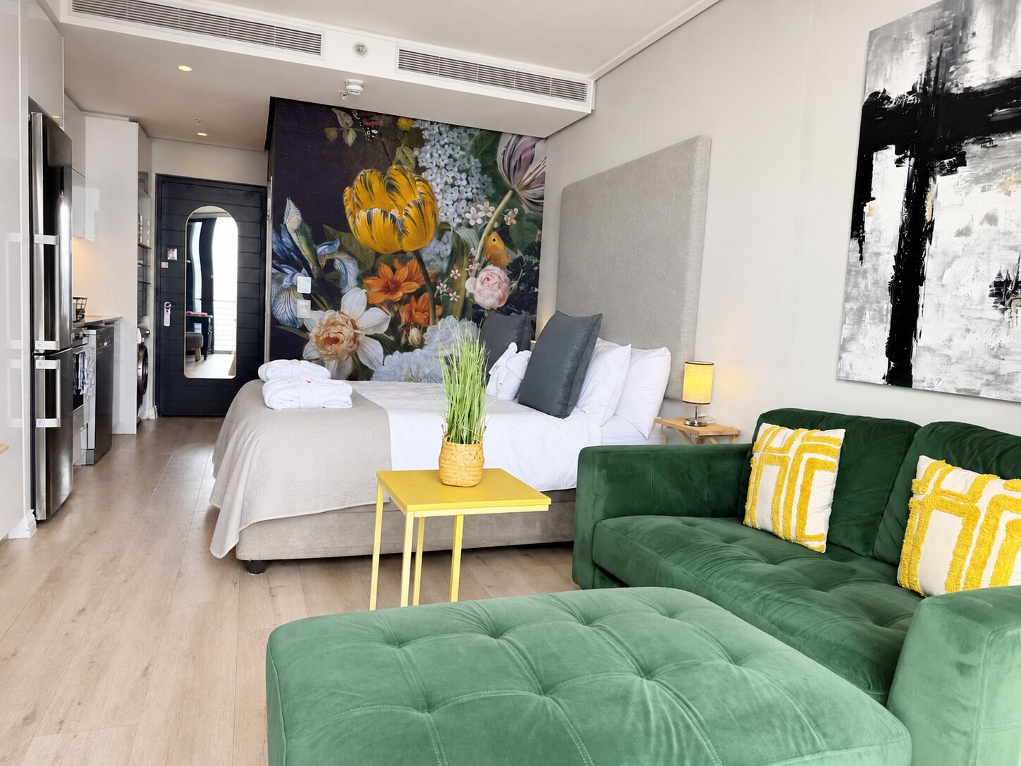 Ein modernes Hotelzimmer mit einem großen Bett, einem grünen Sofa, einem kleinen Tisch mit einer Pflanze und einem Bild an der Wand.