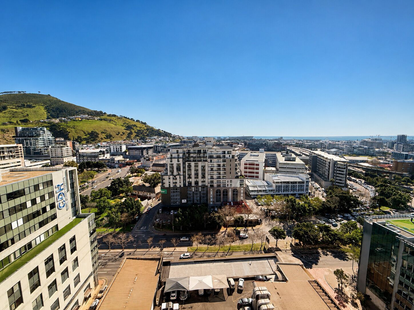 A high-rise building with multiple floors, surrounded by other buildings and a hilly landscape in the background.