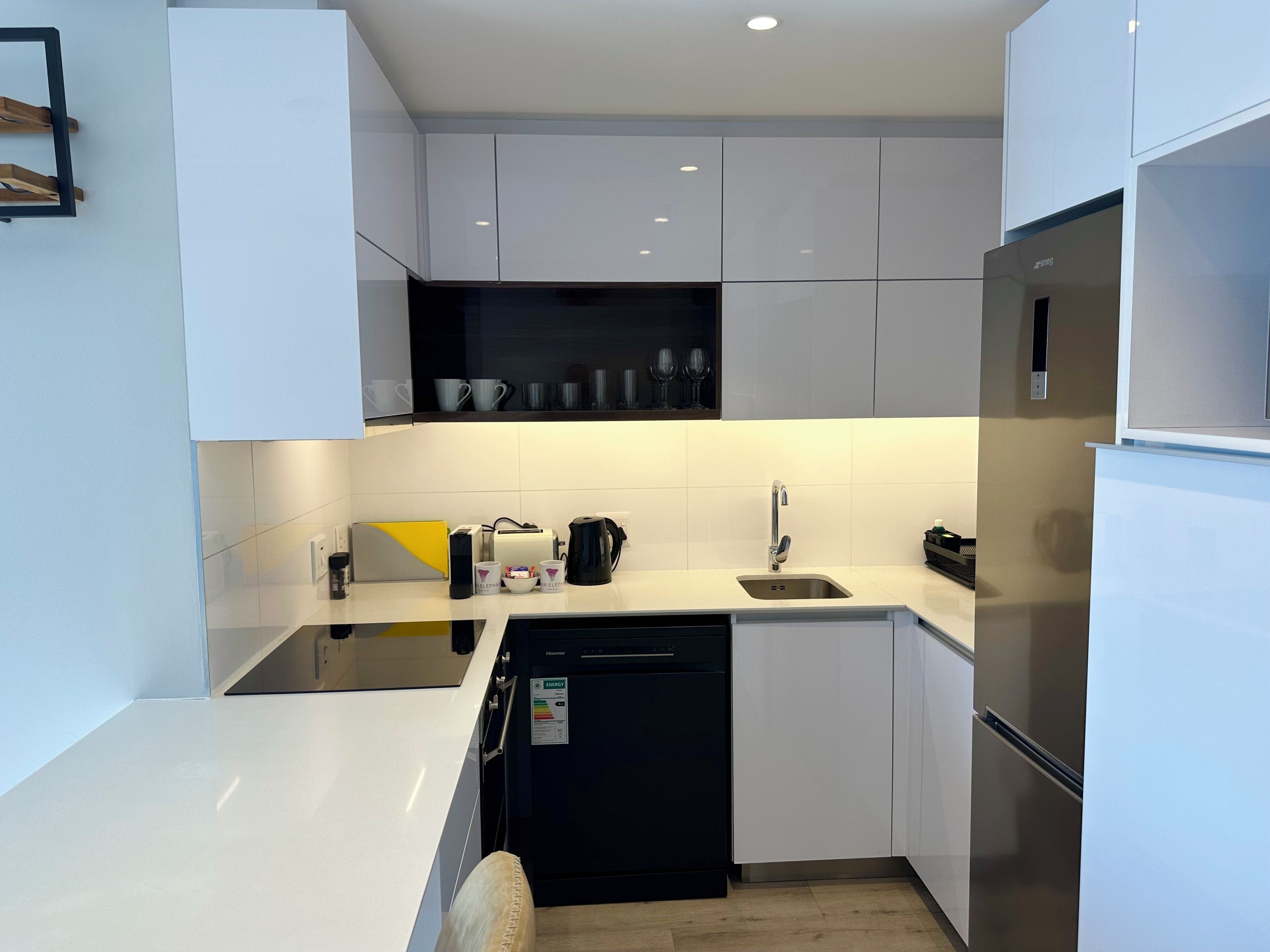 A modern kitchen with white cabinets, a dishwasher, a sink, and a refrigerator.