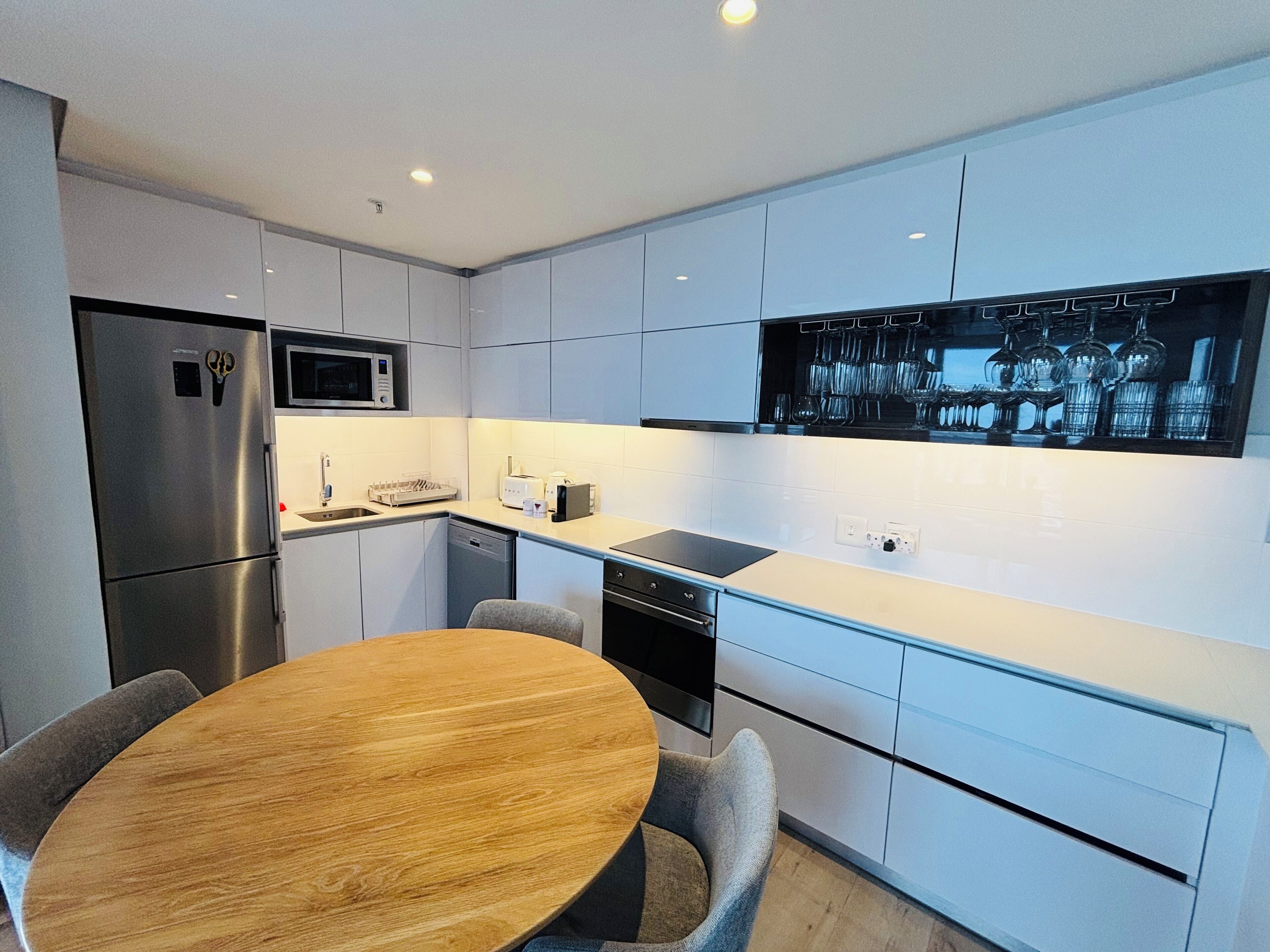 A modern kitchen with white cabinetry, stainless steel appliances, a wooden dining table, and a built-in wine rack.