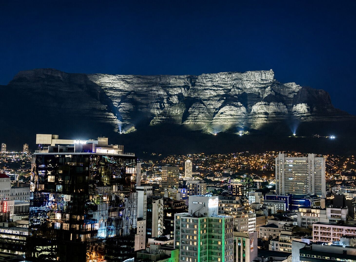 A cityscape with illuminated buildings and a prominent mountain in the background.