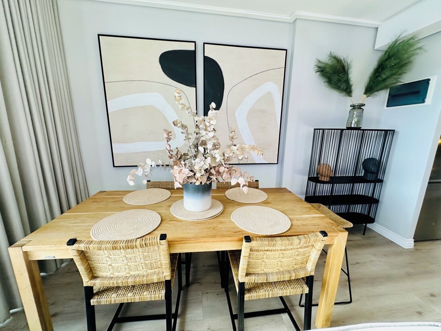 A dining area with a wooden table, woven chairs, and a vase with flowers.