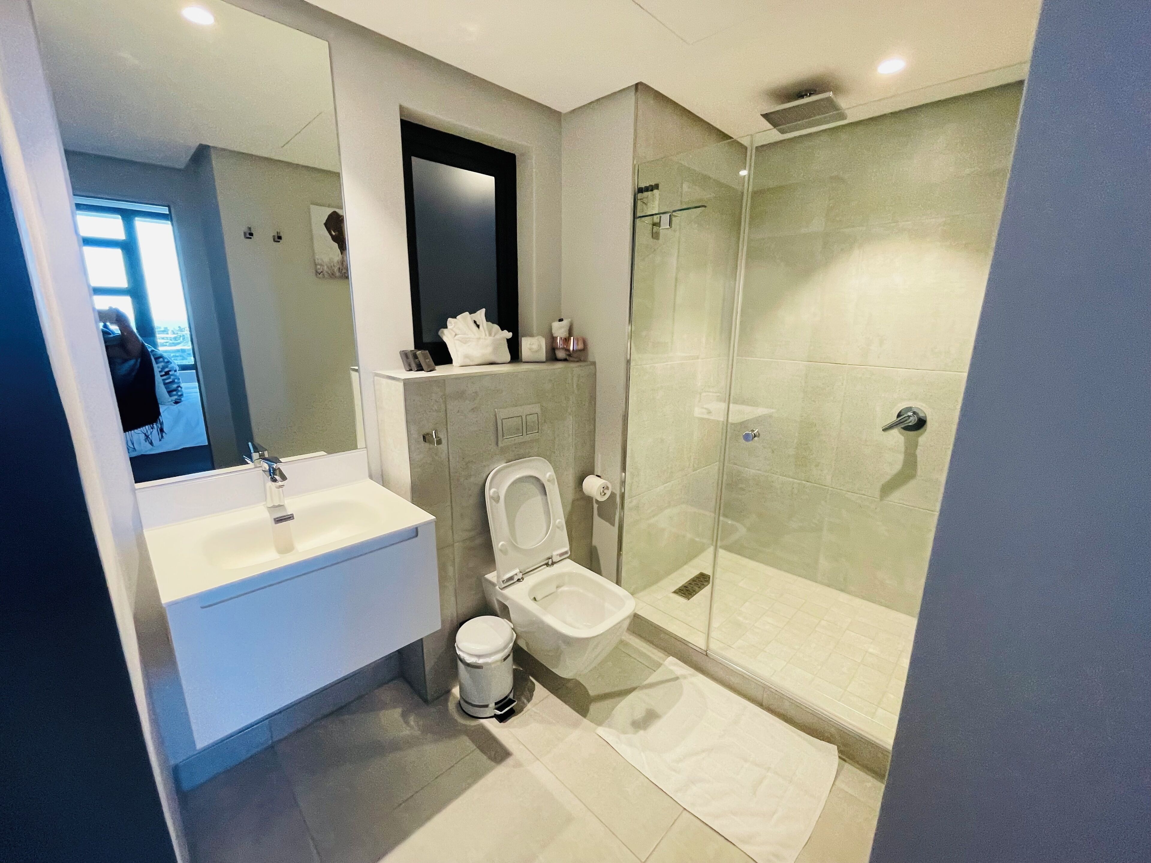 A modern bathroom with a glass-enclosed shower, a white toilet, and a large mirror above a white sink.