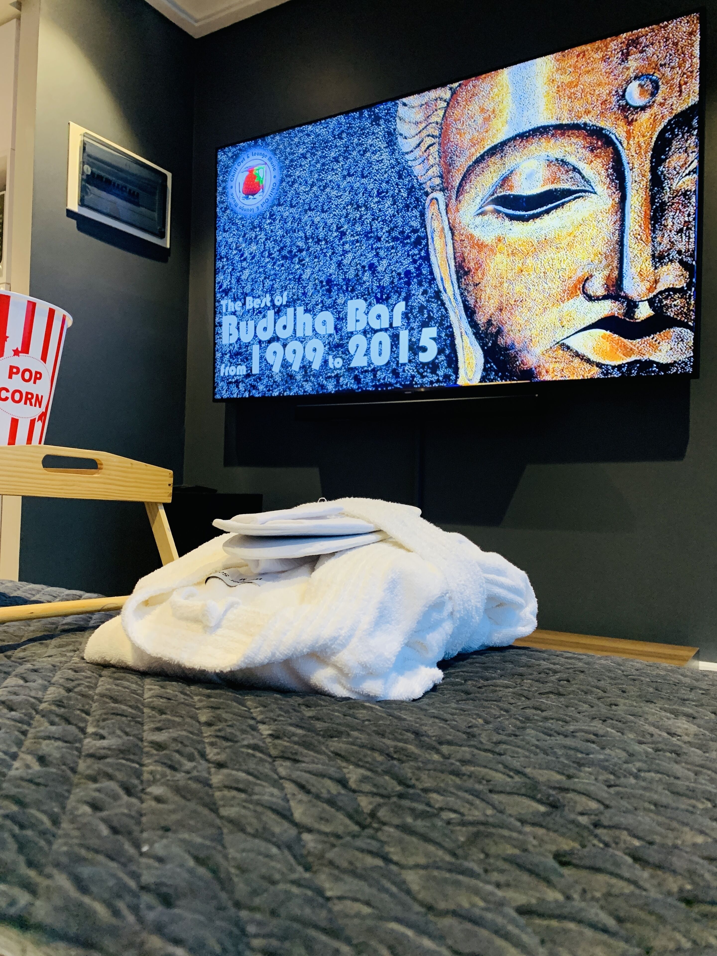 Ein Zimmer mit einem Bett, einem Fernseher, der eine Buddha Bar Veranstaltung zeigt, und einer Popcornschüssel.