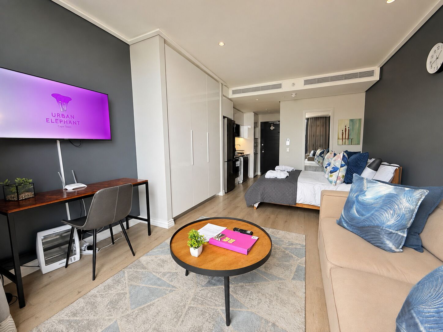 A modern hotel room with a flat-screen TV, a desk, a sofa, and a bed.