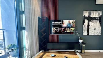 A modern living room with a large TV on a black stand, a wooden coffee table, and a potted plant.