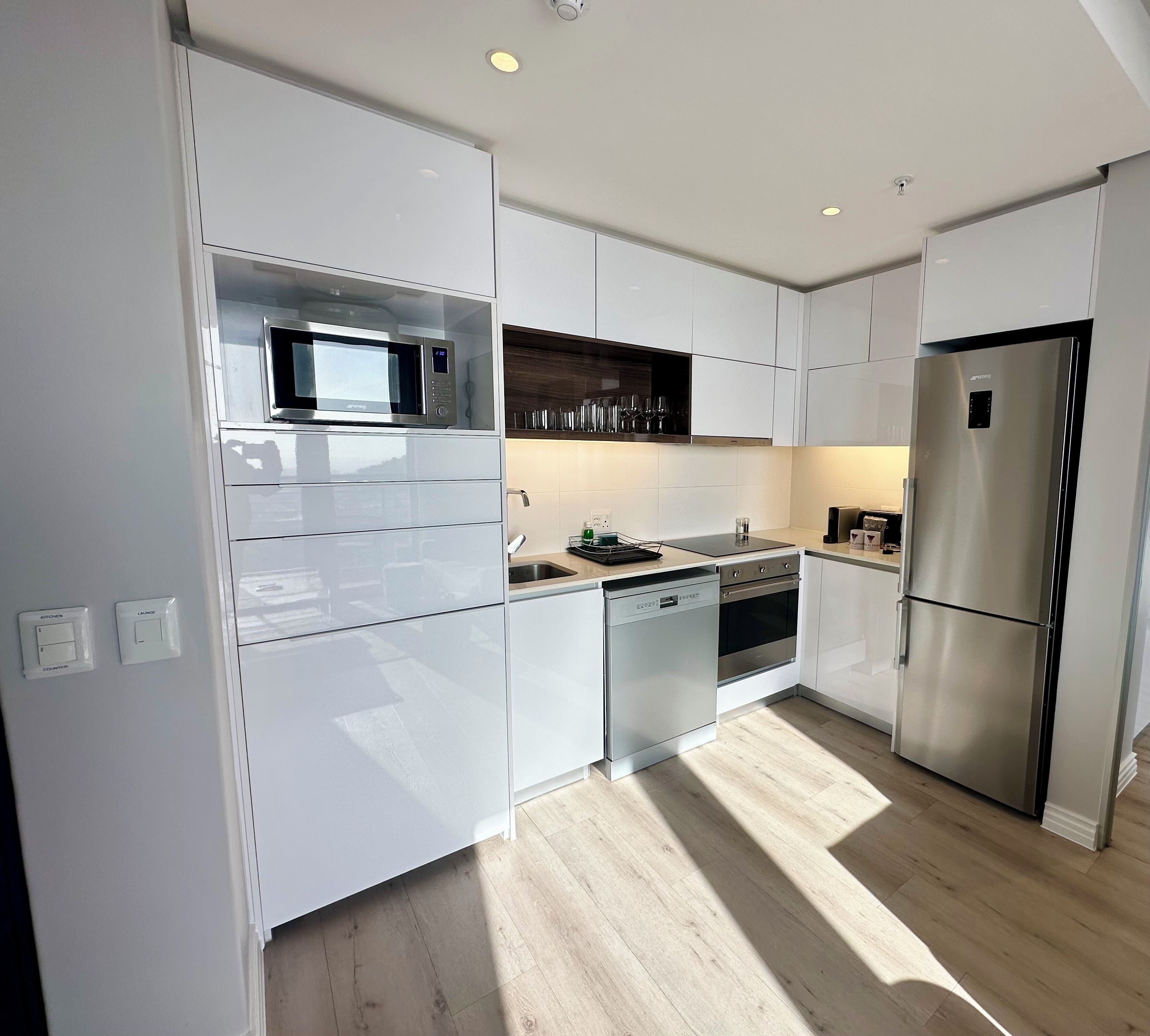 Una cocina moderna con armarios blancos, un refrigerador de acero inoxidable, microondas empotrado y lavavajillas.