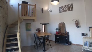 A cozy interior with a wooden staircase, a dining area with chairs and a table, a black cabinet with decorative items, and a white stove. - Logement Entier Avec Terrasse et vue Panoramique (Francillon-sur-Roubion)