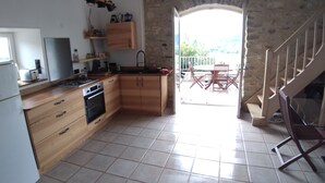 A kitchen with wooden cabinets, a stove, and a microwave. There is a balcony with a table and chairs. - Logement Entier Avec Terrasse et vue Panoramique (Francillon-sur-Roubion)