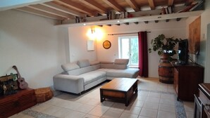 A living room with a sectional sofa, a coffee table, a dartboard, and a guitar on a wooden cabinet. - Logement Entier Avec Terrasse et vue Panoramique (Francillon-sur-Roubion)