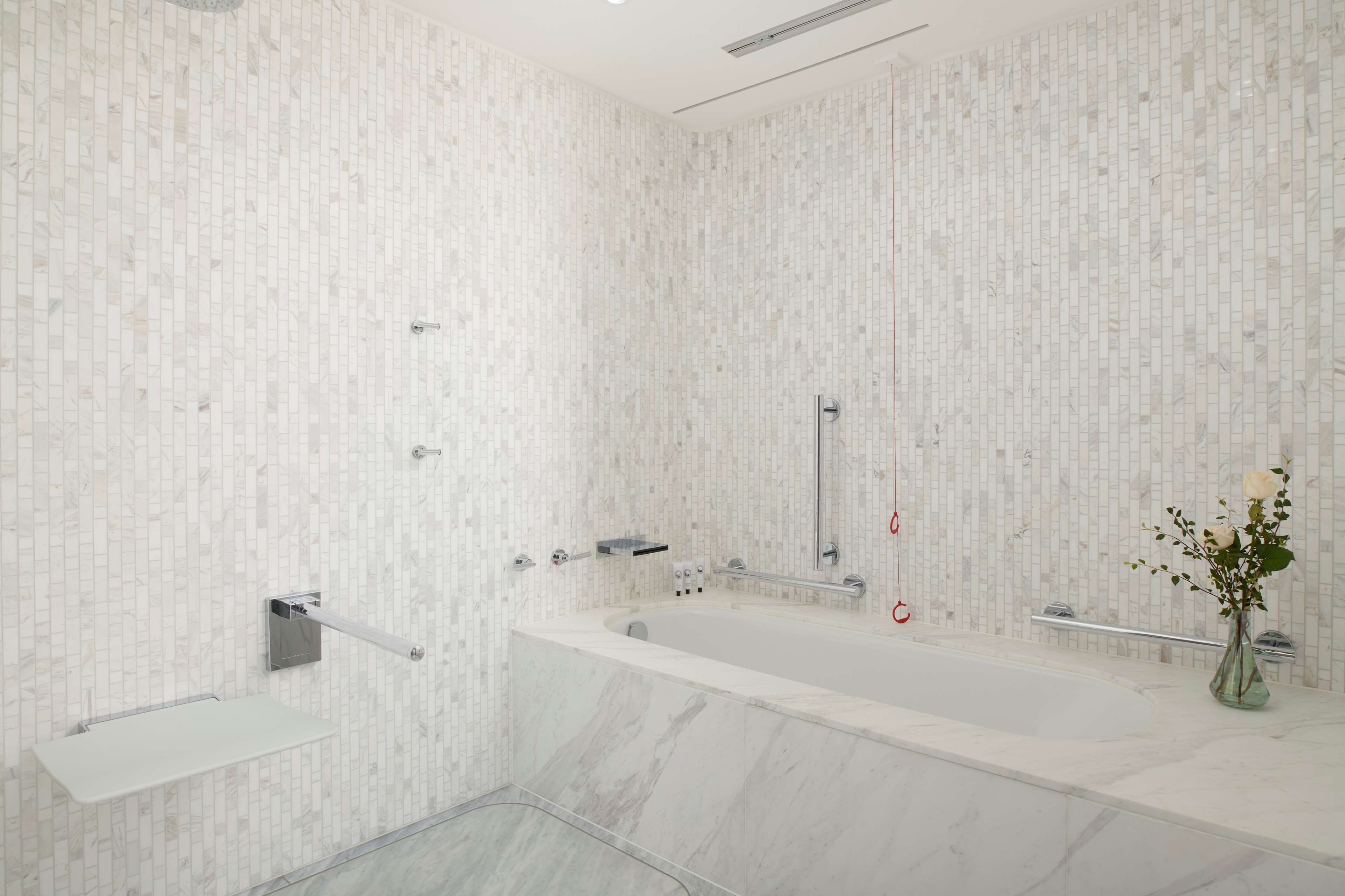 A modern bathroom with a marble bathtub, a glass shower enclosure, and a marble floor.