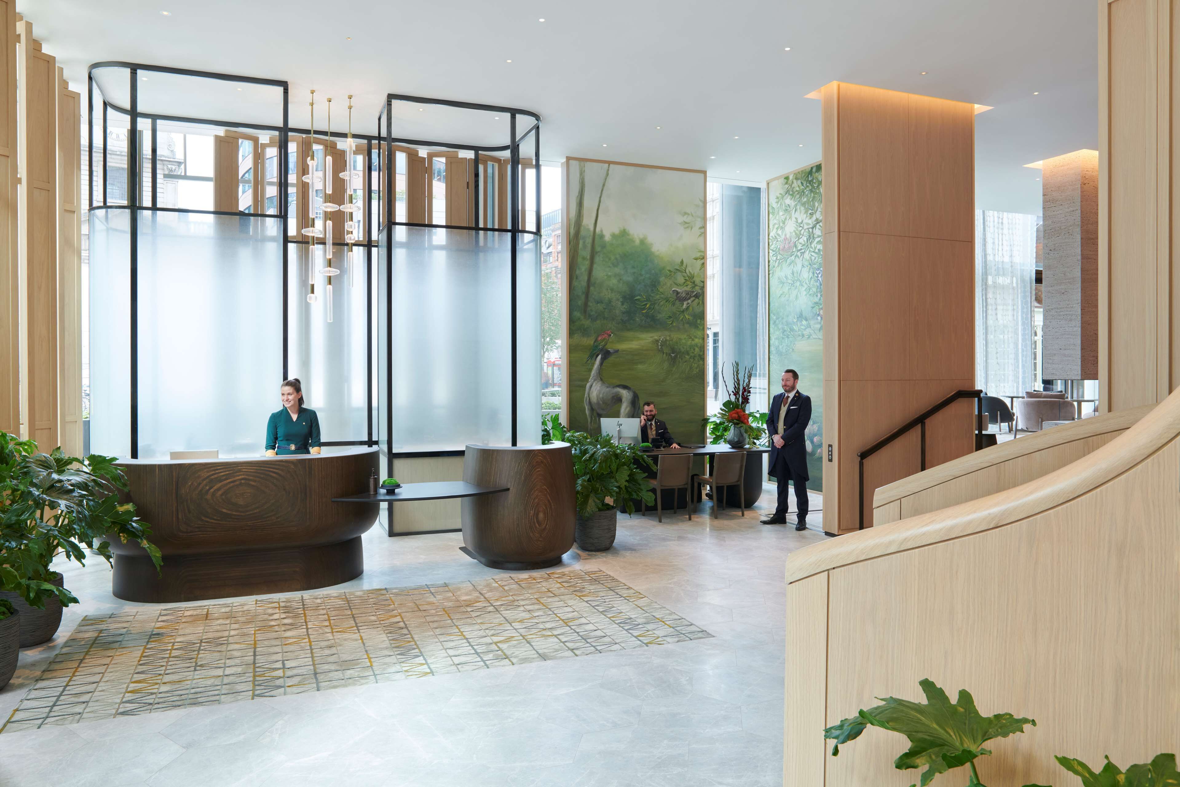 A modern hotel lobby with a reception desk, seating area, and a staircase.