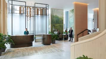 A modern hotel lobby with a reception desk, seating area, and a staircase.