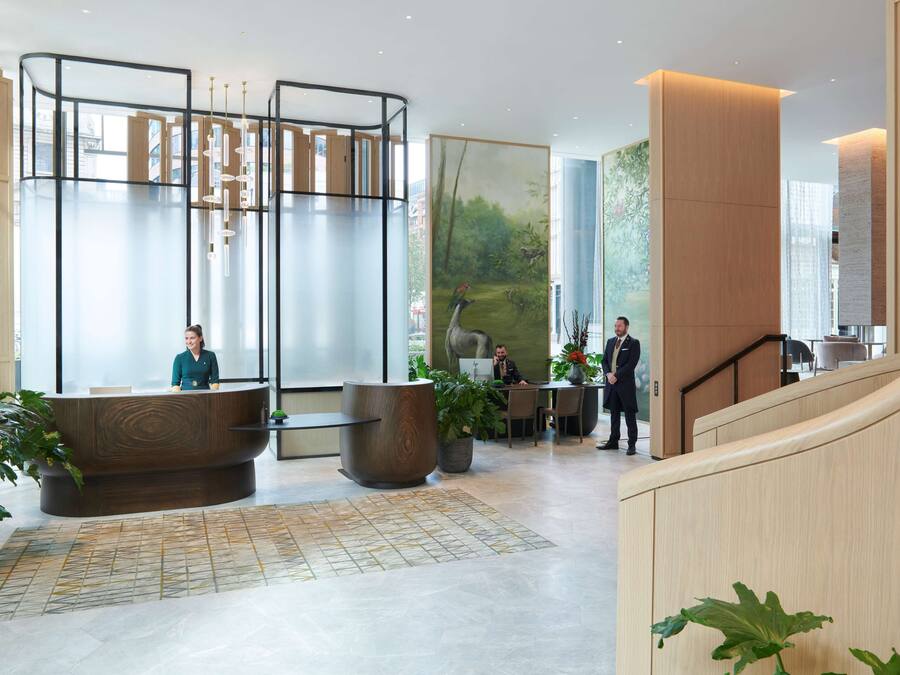 A modern hotel lobby with a reception desk, seating area, and a staircase.
