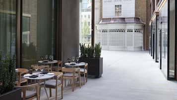 Un área de comedor al aire libre con mesas y sillas, un edificio de ladrillo al fondo y un letrero que dice "STONE HOUSE COURT".