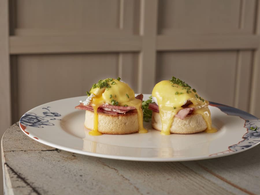 Deux sandwichs aux œufs Bénédicte, présentés sur une assiette ornée d’un motif floral.
