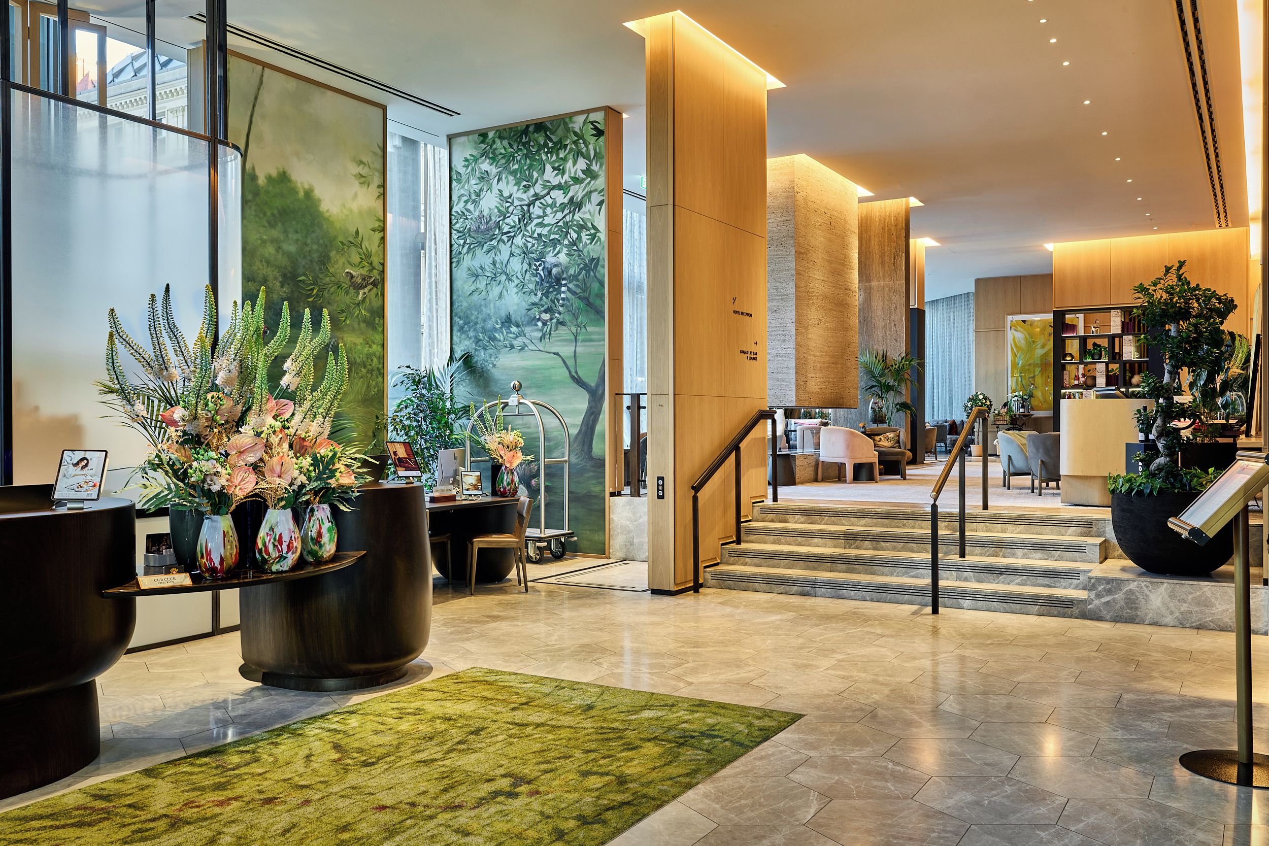 Eine Hotelhalle mit Rezeption, Sitzgelegenheiten und einer Treppe zu den oberen Etagen.