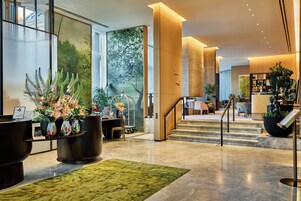 Eine Hotelhalle mit Rezeption, Sitzgelegenheiten und einer Treppe zu den oberen Etagen.