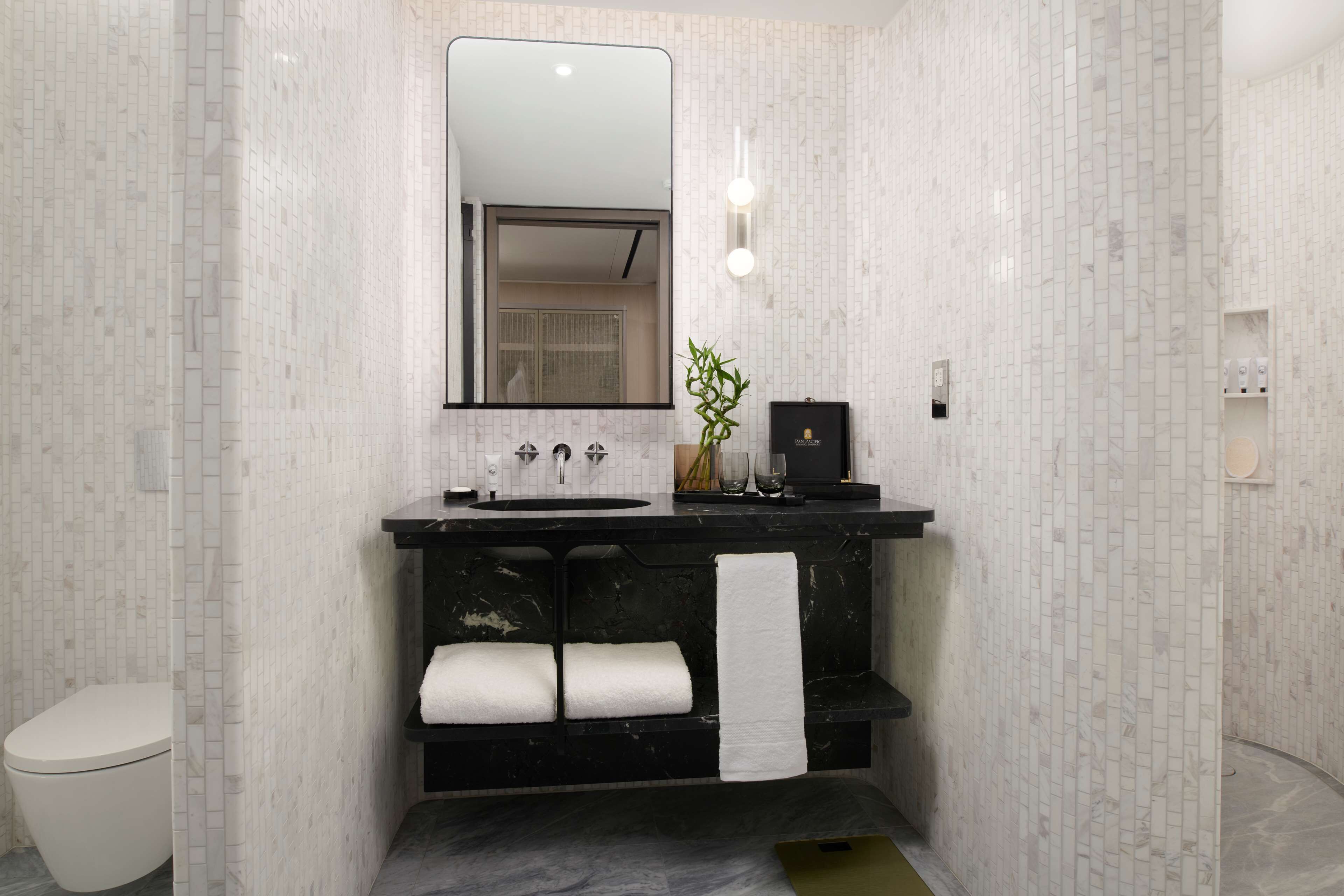 Een moderne badkamer met een zwart wastafelmeubel, witte tegels, een grote spiegel en een toilet.