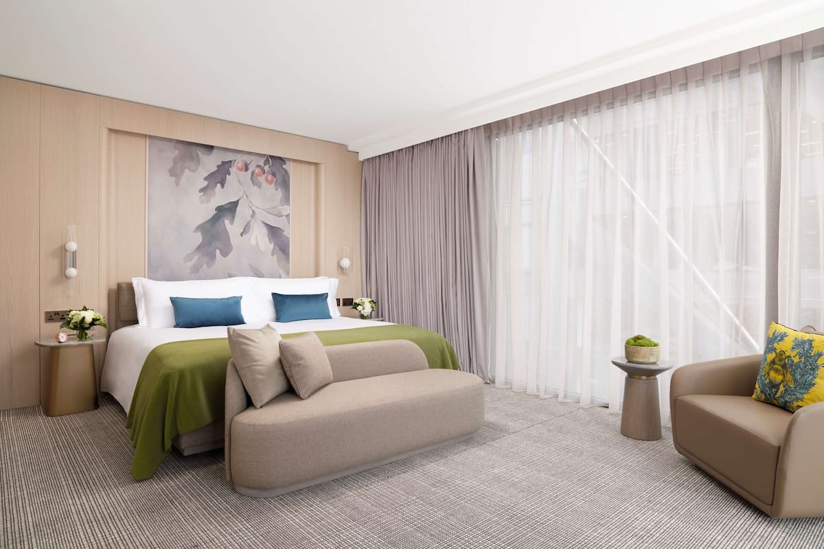 A hotel room with a bed, a sofa, a small table with a plant, and a painting on the wall.