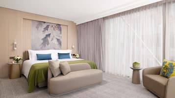 A hotel room with a bed, a sofa, a small table with a plant, and a painting on the wall.