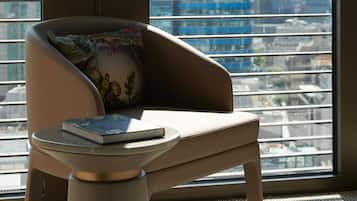 A modern chair with a cushion and a small table with a book, positioned in front of a large window with a city view.