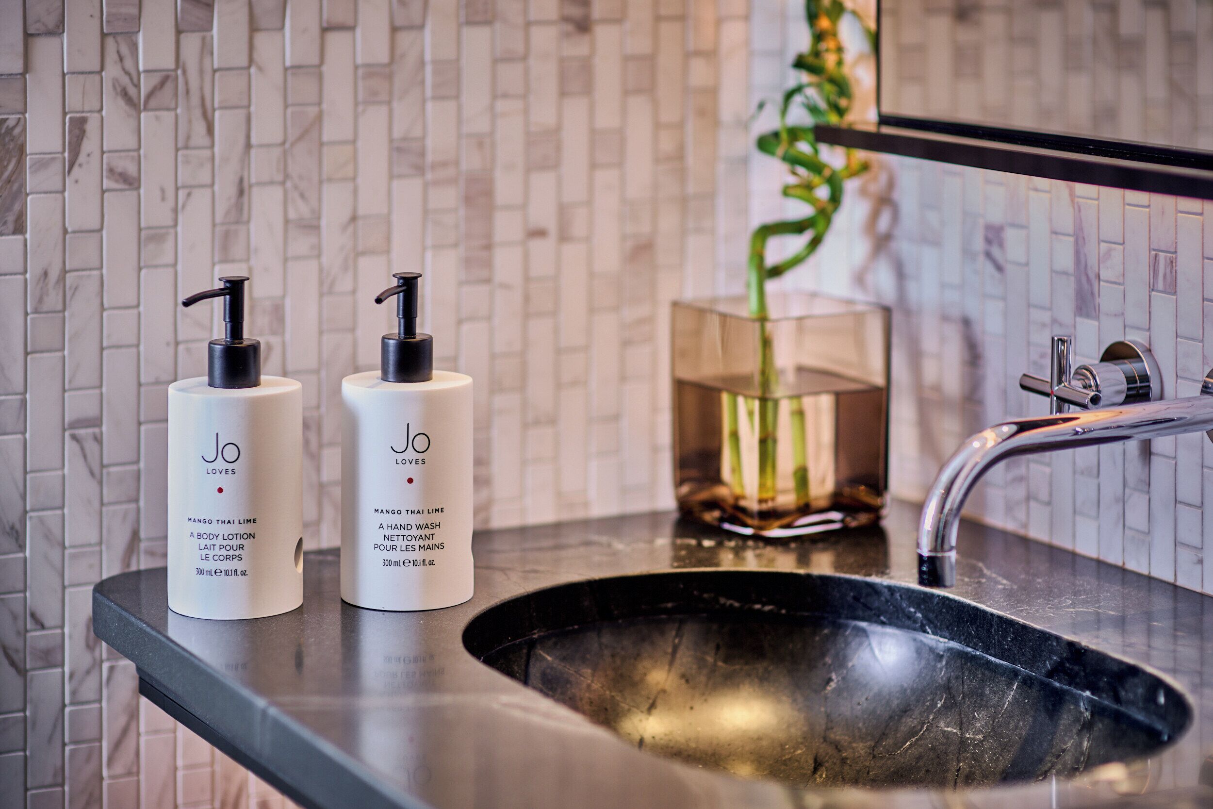 A bathroom with a black sink, two white lotion bottles, and a glass vase with a plant.