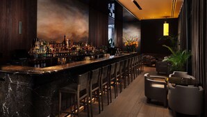 A bar area with a long counter, multiple stools, and a variety of bottles. - Pan Pacific London (London)