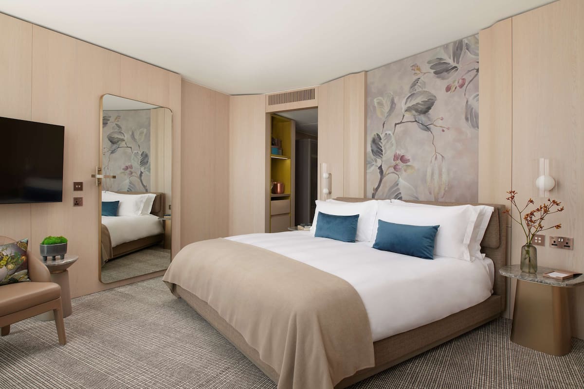 A modern hotel room with a large bed, a flat-screen TV, a small seating area, and a mirror.