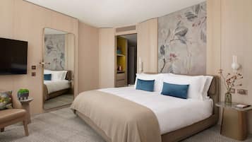 A modern hotel room with a large bed, a flat-screen TV, a small seating area, and a mirror.