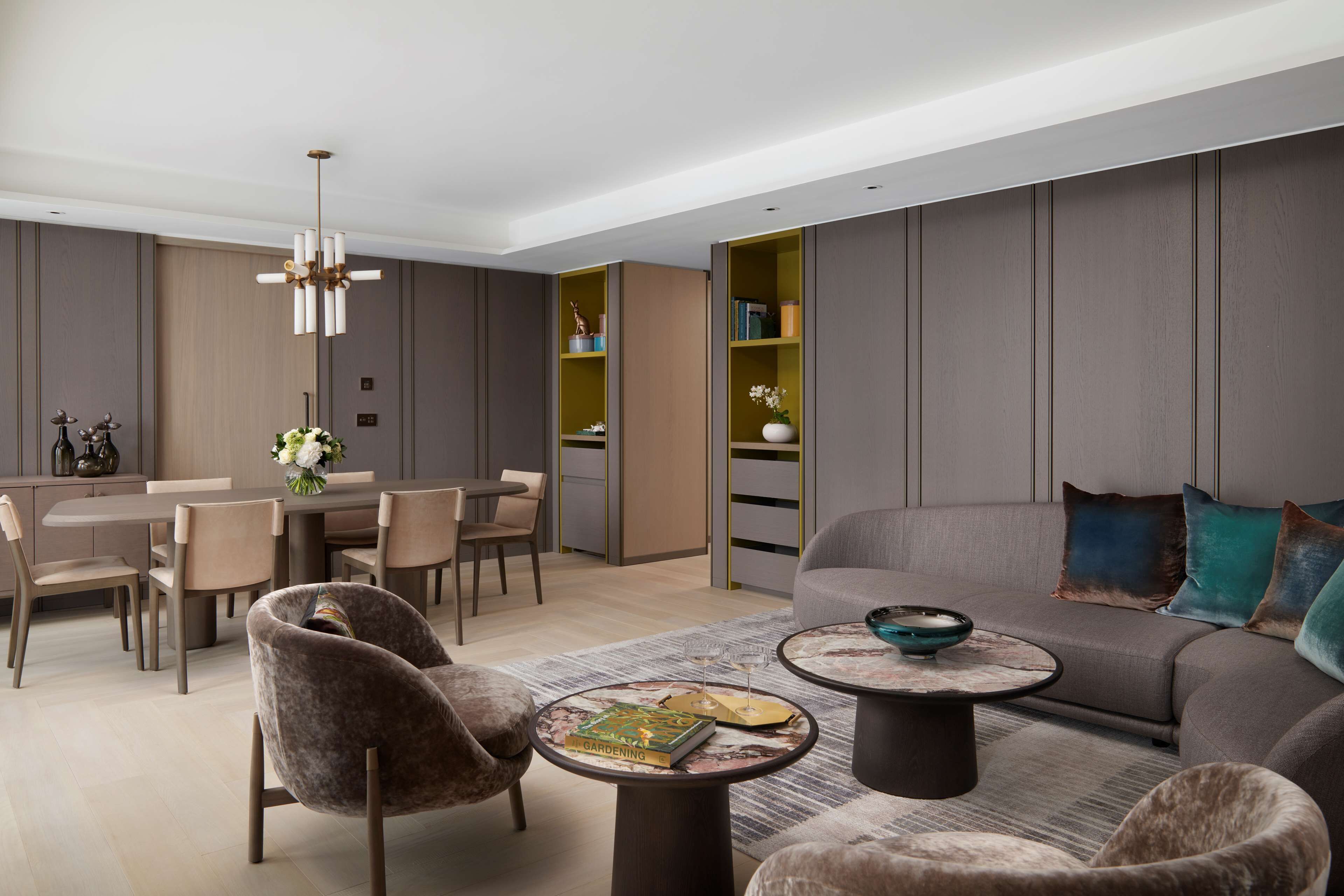 A modern living room with a sofa, armchairs, a dining table, and a bookshelf.