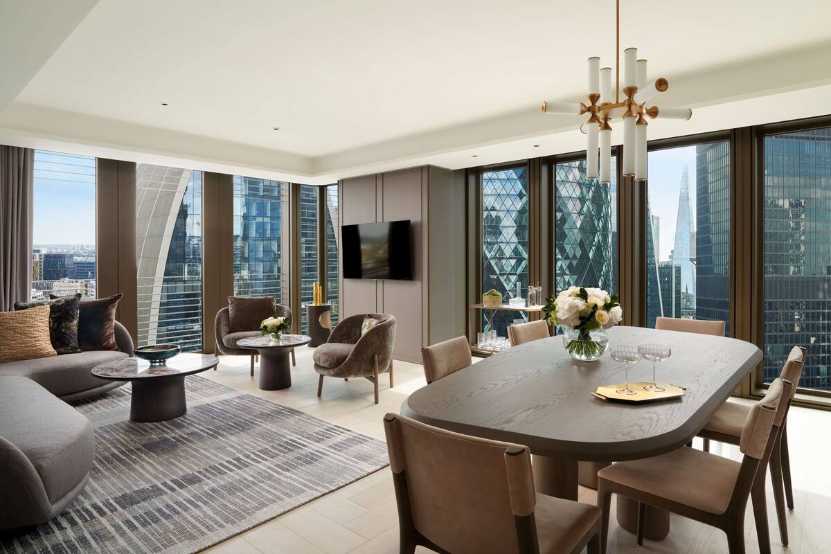 A modern living room with a large dining table, comfortable seating, a flat-screen TV, and large windows offering city views.