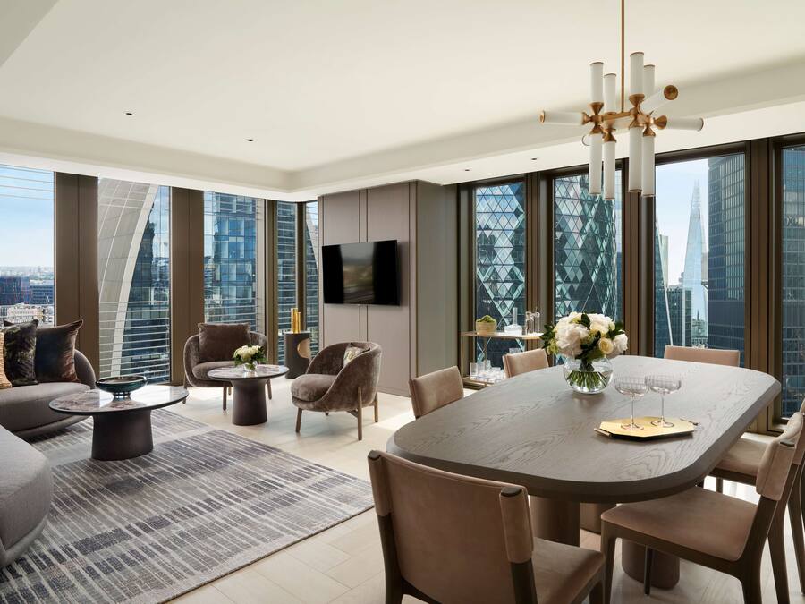 A modern living room with a large dining table, comfortable seating, a flat-screen TV, and large windows offering city views.