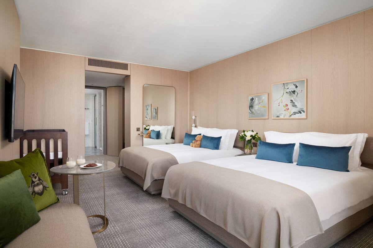 A hotel room with two beds, a small table, a sofa, and a TV.