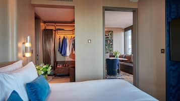 A hotel room with a large bed, a sitting area with a sofa and a small table, a bathroom with a shower and a mirror, and a view of the outside through a large window.