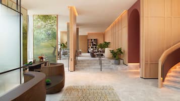 A modern hotel lobby with a curved reception desk, a staircase leading to the upper floor, and a large painting on the wall.