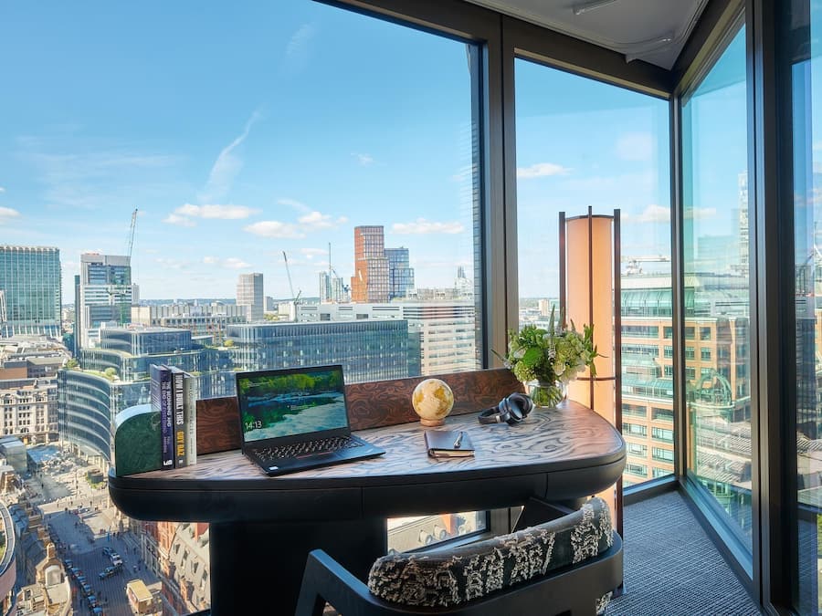 Un espacio de oficina moderno con una computadora portátil, libros, un globo terráqueo y auriculares sobre una mesa de madera con vistas a la ciudad.