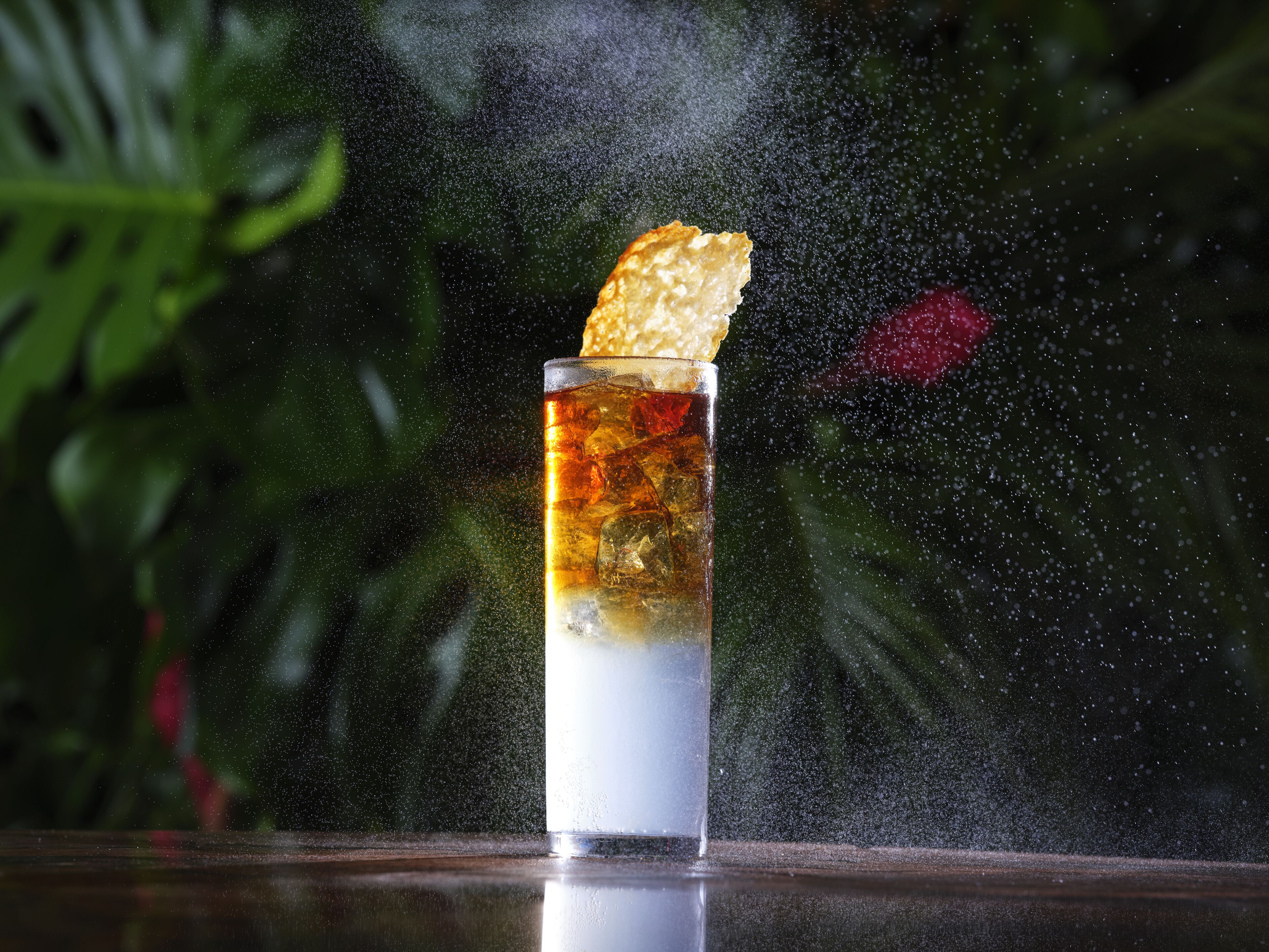 Un verre contenant un liquide transparent, des glaçons et une garniture, le tout posé sur une surface réfléchissante.