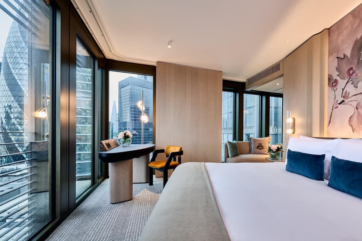 A modern hotel room with a large bed, a desk, and a view of the cityscape.