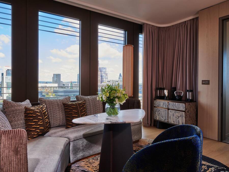 Un salon moderne avec un canapé, une table basse et une vue sur le paysage urbain grâce à de grandes fenêtres.