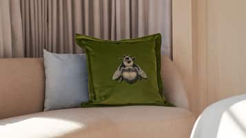 A corner of a room with a beige sofa, a green pillow with a fly design, and a light-colored wall.