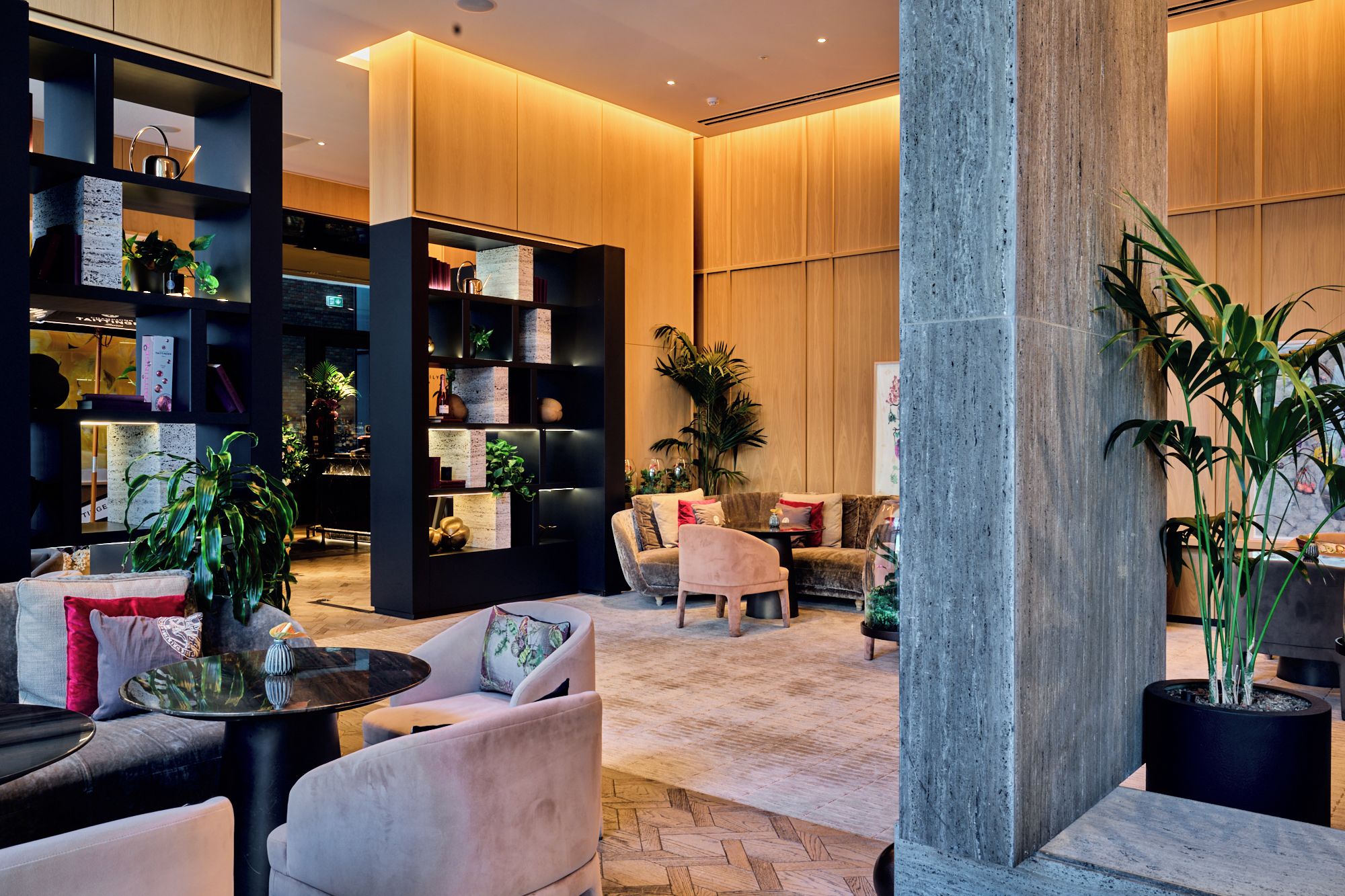 Eine moderne Hotelhalle mit Sitzgelegenheit, einer großen Bücherwand und einer Säule mit Pflanzgefäß.