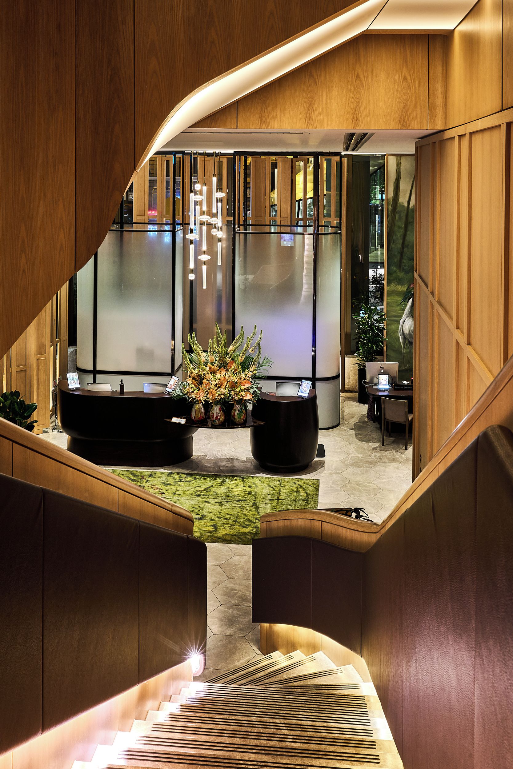 A modern hotel lobby with a reception desk, seating area, and a staircase leading to upper floors.