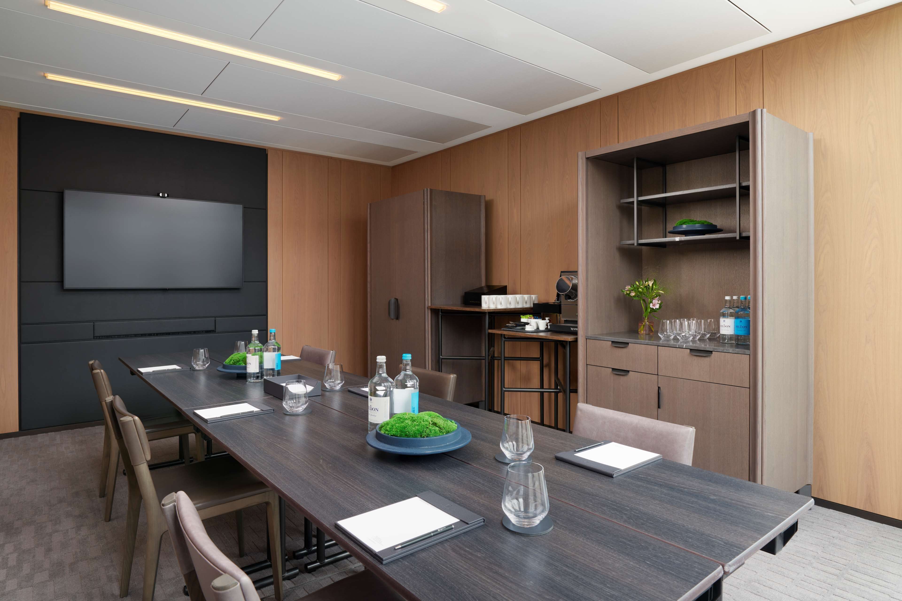 A modern conference room with a long table, chairs, a flat-screen TV, and built-in shelving.