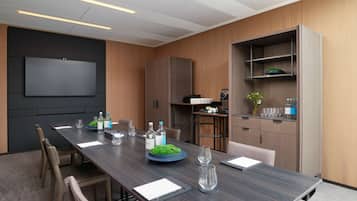 A modern conference room with a long table, chairs, a flat-screen TV, and built-in shelving.