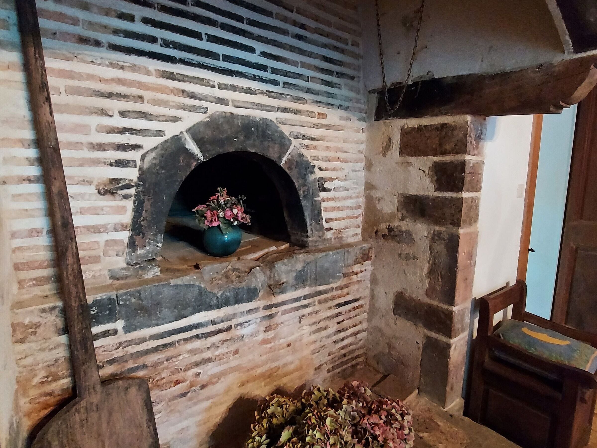 A rustic brick fireplace with a flower vase, a wooden chair, and a stone bench.