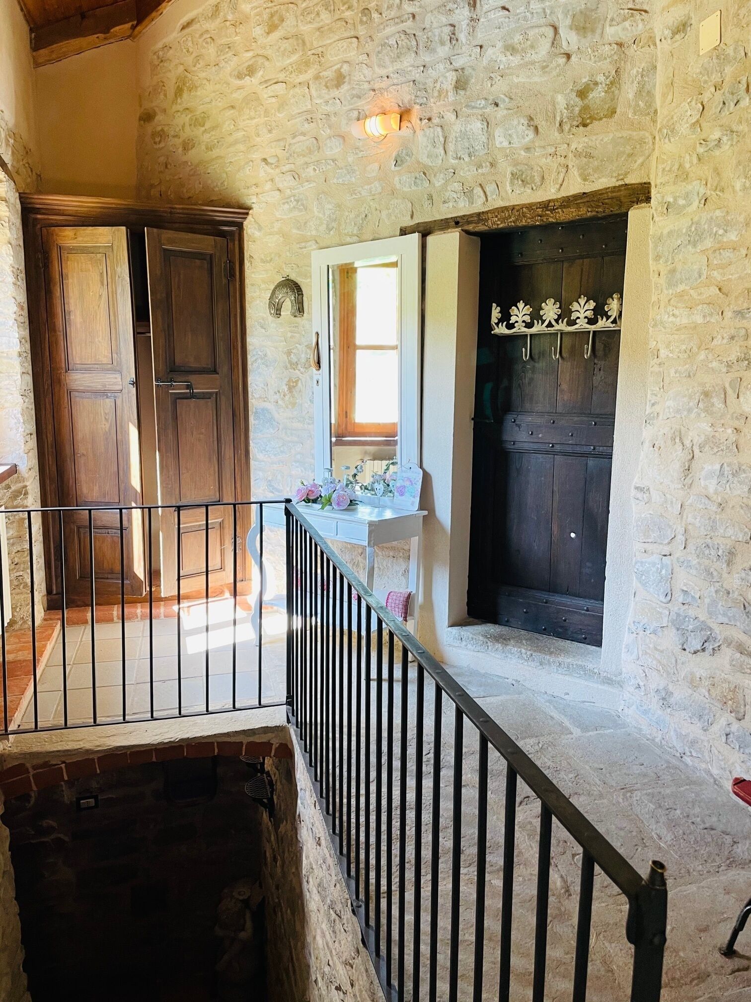 A stone-walled room with a wooden door, a white table with flowers, and a black railing.